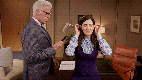 An animated gif from a scene of The Good Place in which Michael, a man in a suit, tries to examine the ear of Janet, a person in a vest and a blouse. When the tool is put into Janet's ear, a rainbow emanates from her other ear.